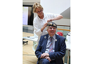 Uniklinik-Mitarbeiterin Anne-Katrin Baum legt Minister Möllring das innovative und leicht zu handhabende EEG-Headset an.
Ministerium für Wissenschaft und Wirtschaft/Franziska Krüger